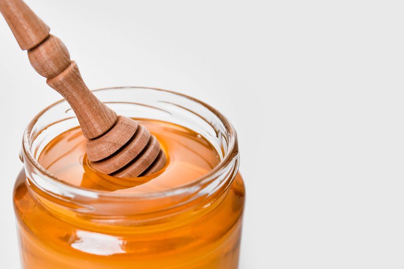 A glass jar of honey with a wooden dipper
