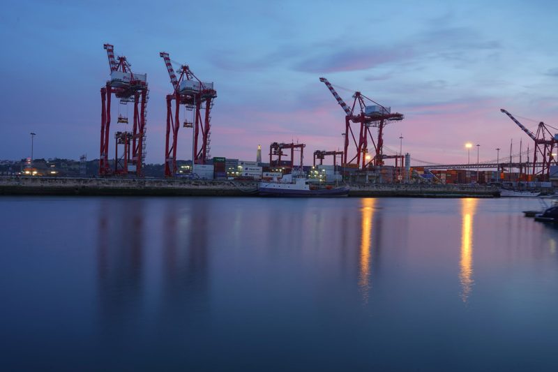 Container cranes silhouetted against a sunset over calm water